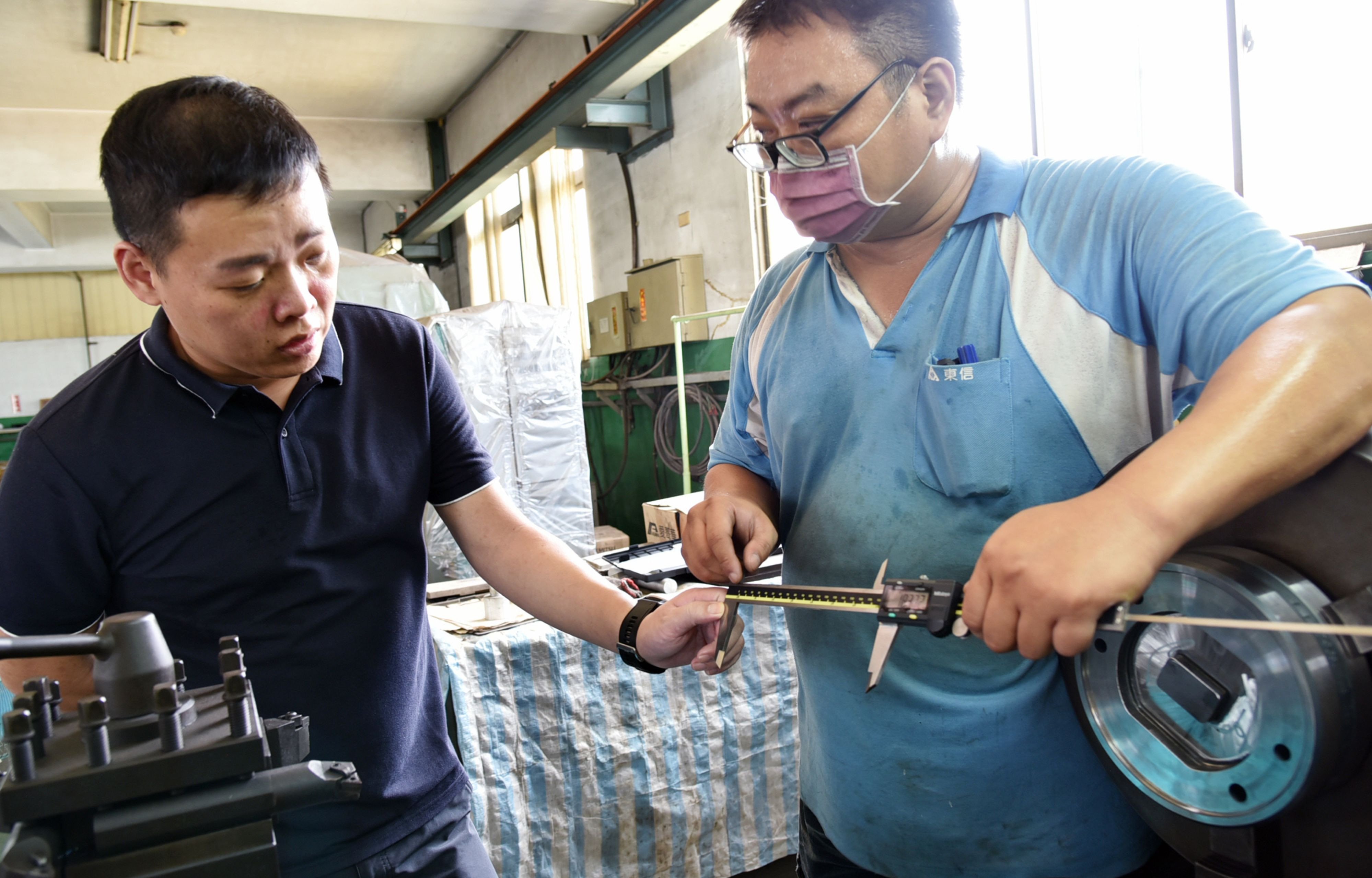 東信輕金屬董事長林彥伯(左)關心員工使用輔具(數位卡尺)狀況。