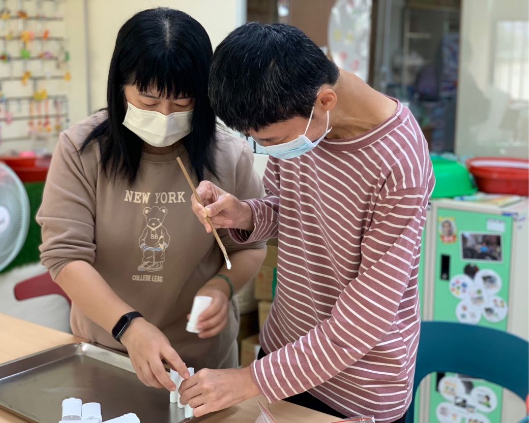 蔡惠名(左)教導慢飛天使製作產品，與孩子們相處融洽，她也說工作很有意義。